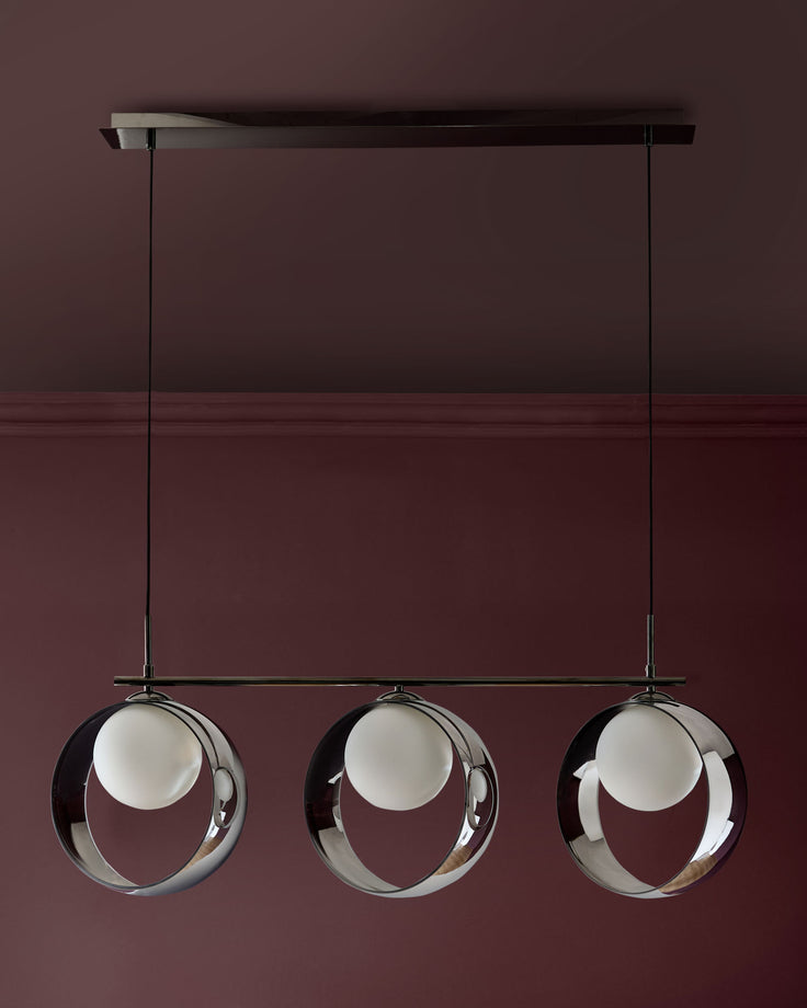 Chloe 3-pendant light with chrome frame and frosted glass spheres suspended from black bar mount against burgundy wall.