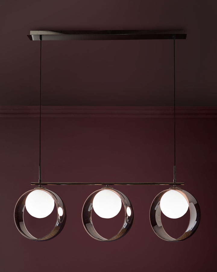 Chloe 3-pendant light with spherical glass shades and chrome finish, suspended from black rod against burgundy wall.
