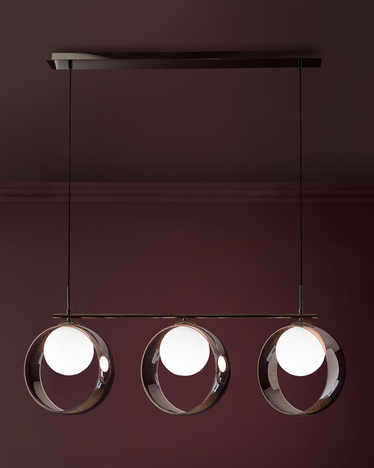 Chloe 3-pendant light with spherical glass shades and chrome finish, suspended from black rod against burgundy wall.