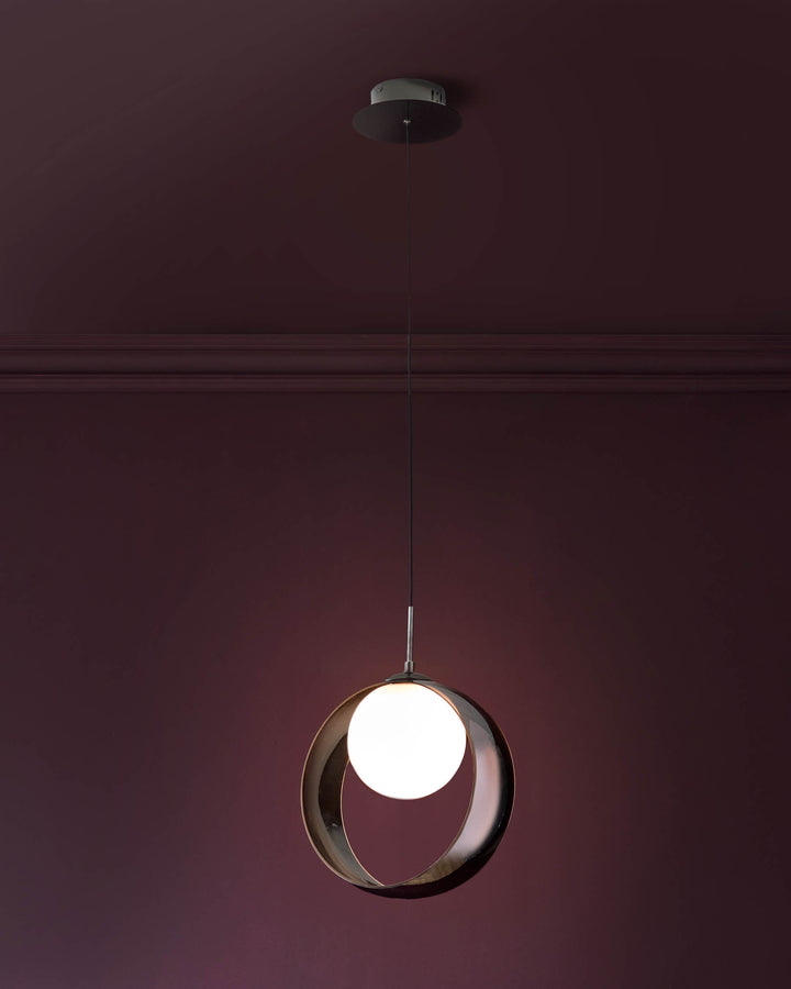 Spherical pendant light with chrome metal frame and glowing white glass globe, suspended from ceiling against burgundy wall.