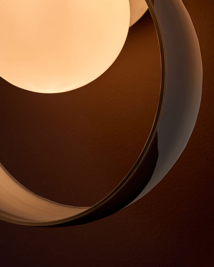 Chloe wall light with curved glass shade in warm amber tone and chrome finish, shown at angle highlighting sculptural form.