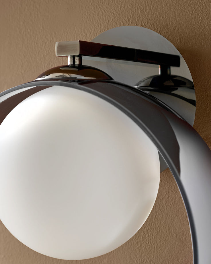 Chloe wall light with frosted glass globe shade, chrome and silver metal fixture, mounted on beige wall.
