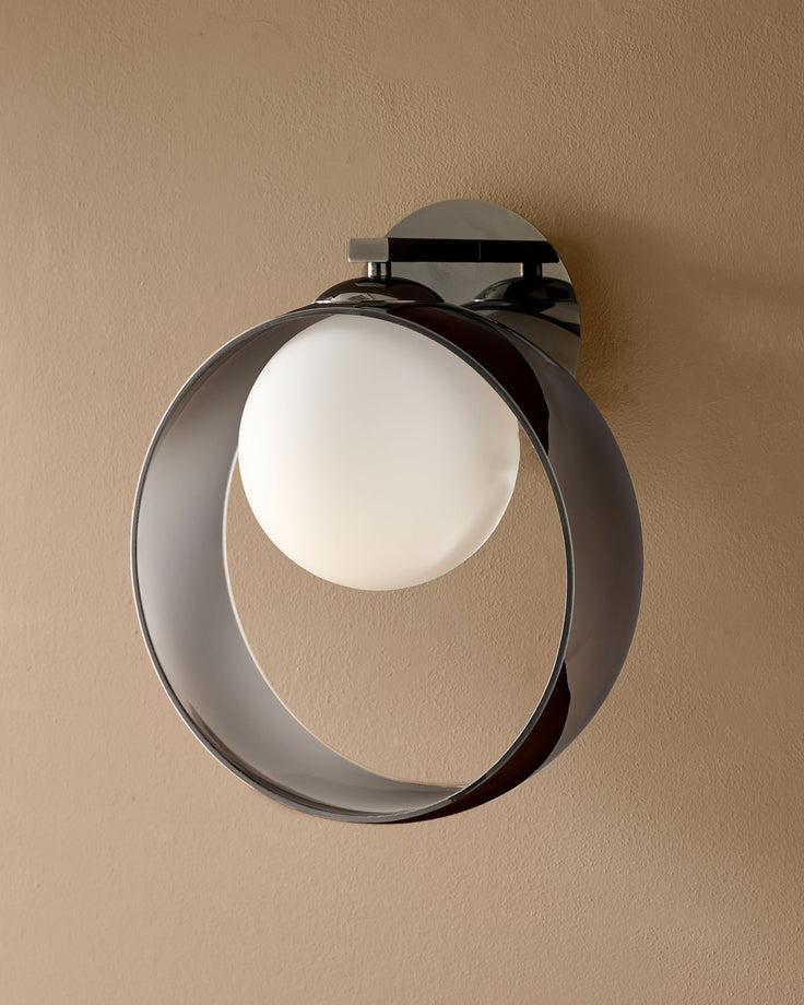 Chloe wall light with curved chrome frame and frosted glass sphere, mounted on beige wall.