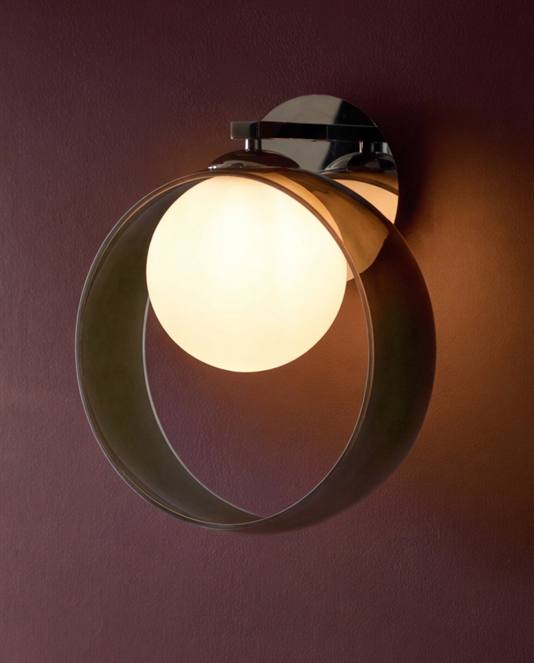 Chloe wall light with curved green glass shade and chrome mounting bracket, illuminated against burgundy wall.