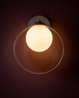 Chloe wall light with spherical opal glass shade and dark metal fixture mounted on wall, glowing warm light.
