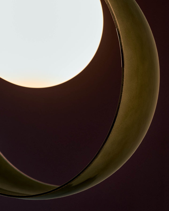Green glass pendant light with curved organic shape and warm interior glow, close-up detail view.