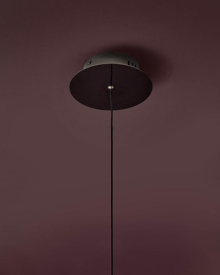 Black disc pendant light with thin cord suspension against mauve wall.