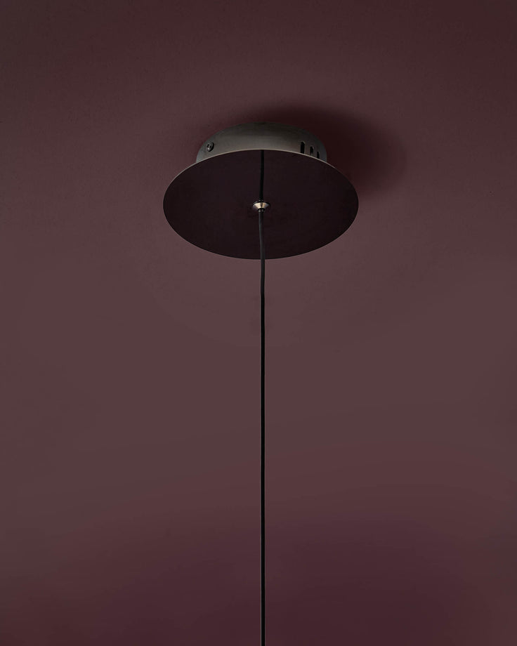 Black disc pendant light with thin cord suspension against mauve wall.