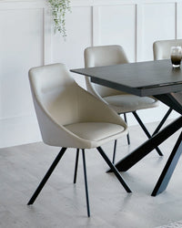 Modern minimalist dining room furniture featuring a dark wood table with a sleek, black frame and angular legs, accompanied by light grey upholstered chairs with comfortable curved backs and slender, tapered black metal legs.
