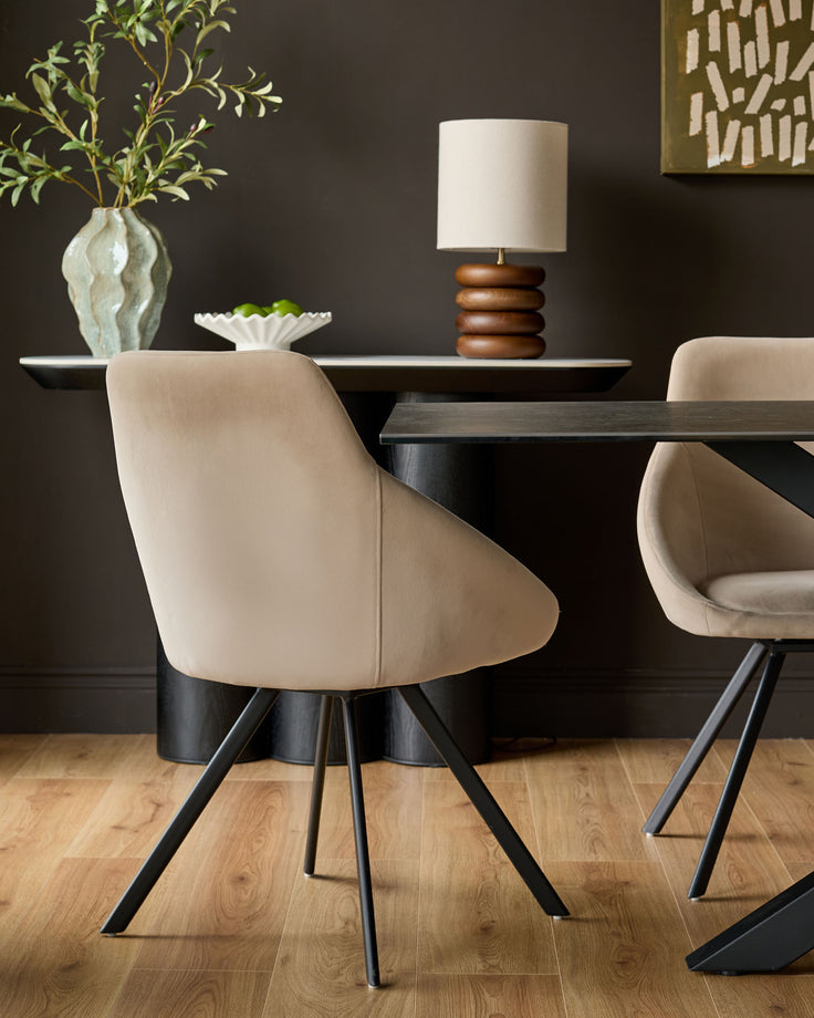 Champagne velvet swivel chair with curved back and black metal legs, shown in dining setting.