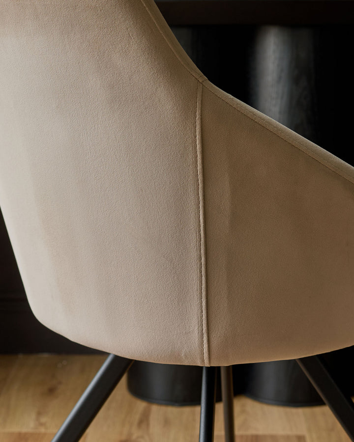 Cleo velvet swivel chair in champagne, close-up of curved backrest and black metal base on wooden floor.