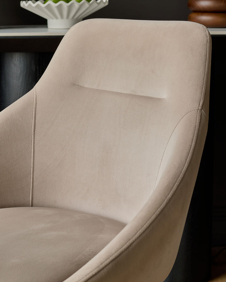 Champagne velvet swivel chair with curved backrest and armrests, shown at an angle against a dark desk.