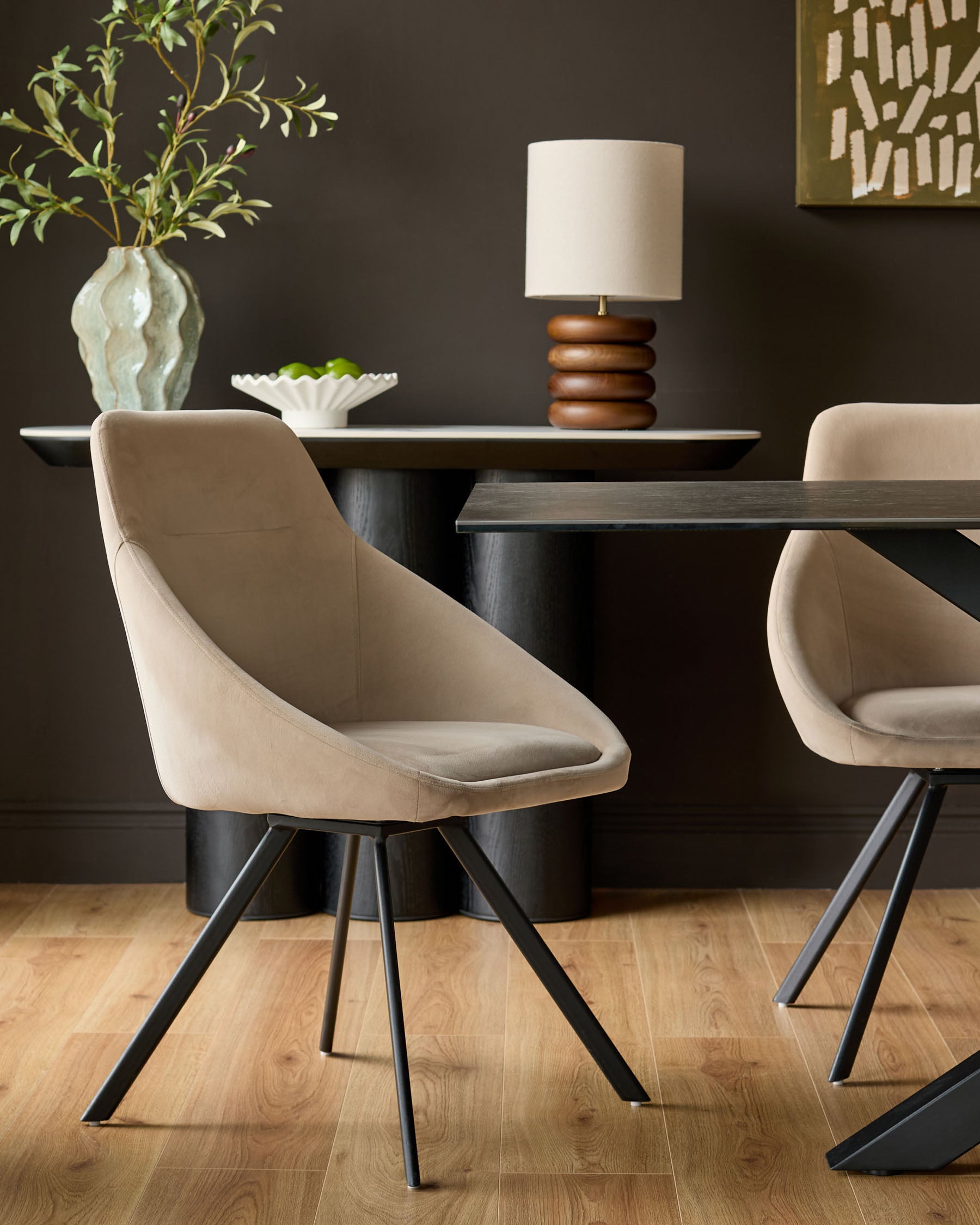 Champagne velvet swivel chair with curved bucket seat and black metal legs, shown in dining room setting.