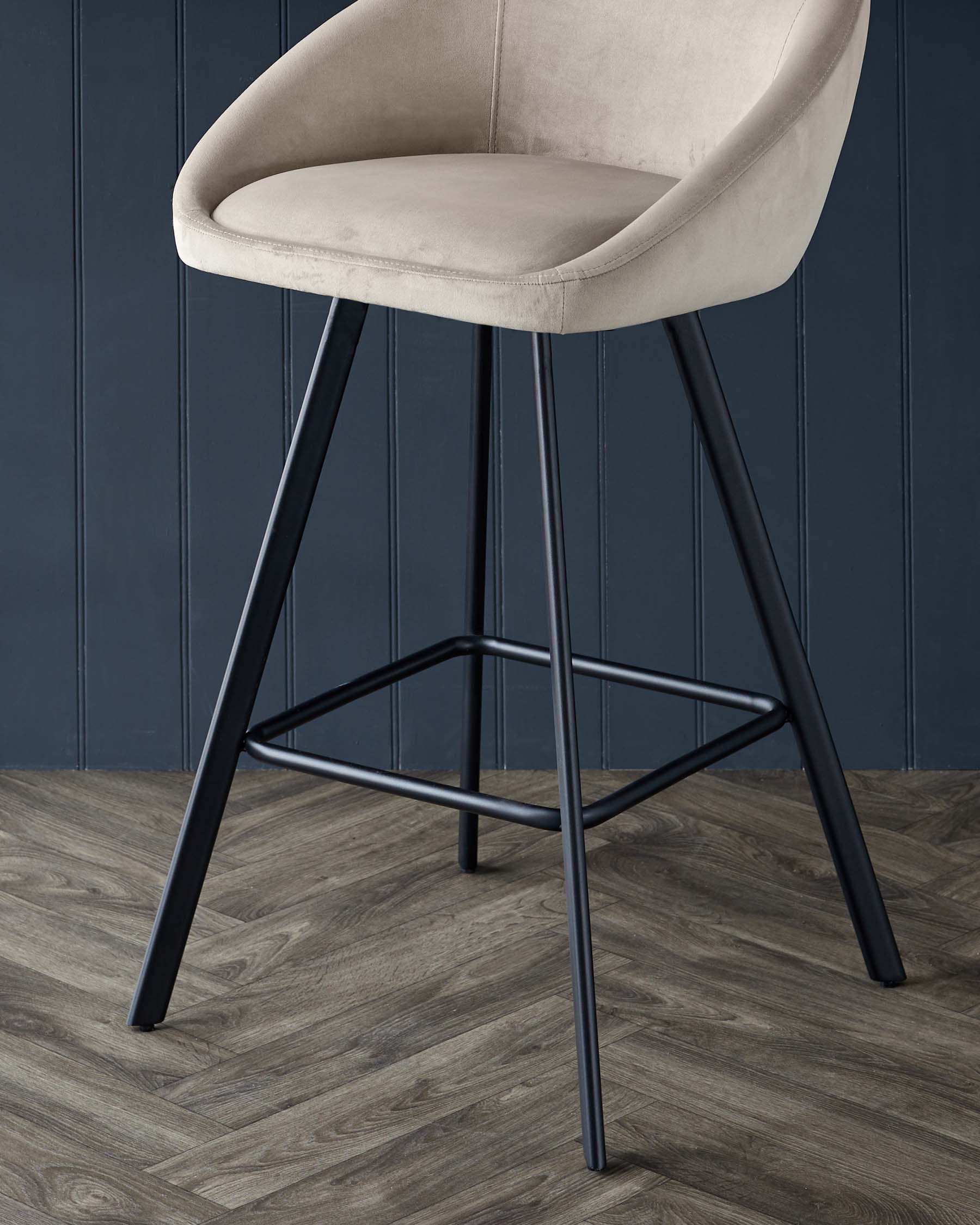 A stylish, tan velvet bar stool with sleek black metal legs against a dark blue panelled wall and wooden floor.