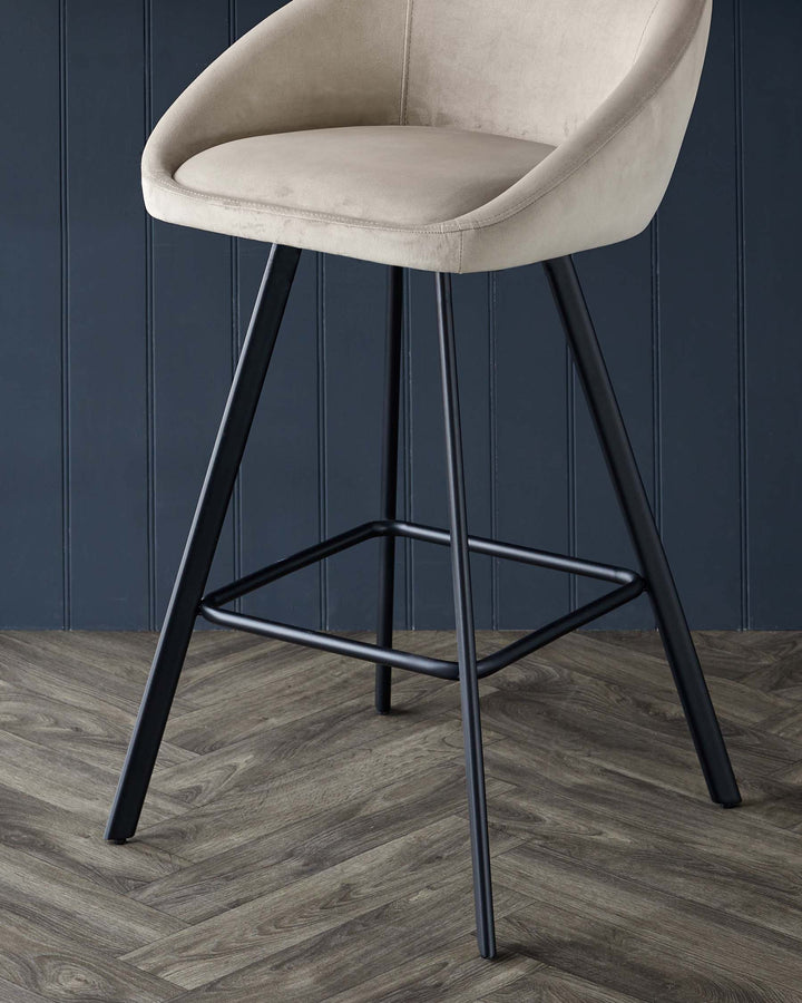 A stylish, tan velvet bar stool with sleek black metal legs against a dark blue panelled wall and wooden floor.