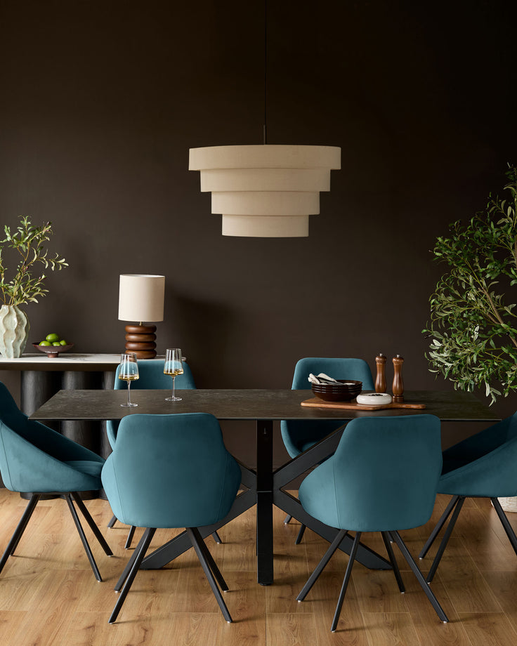 Cleo dark teal velvet swivel chair with curved back and black tapered legs, shown at dining table.
