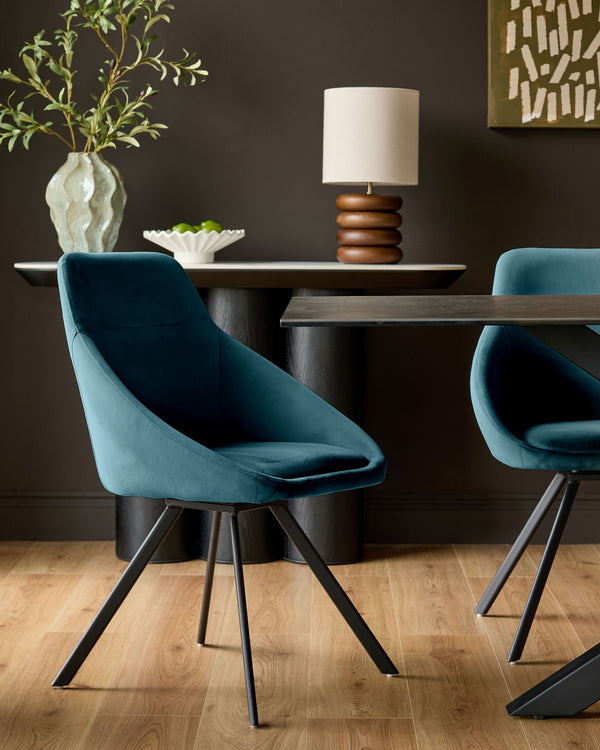 Dark teal velvet swivel chair with curved bucket seat and black angled legs, shown in a modern dining room setting.