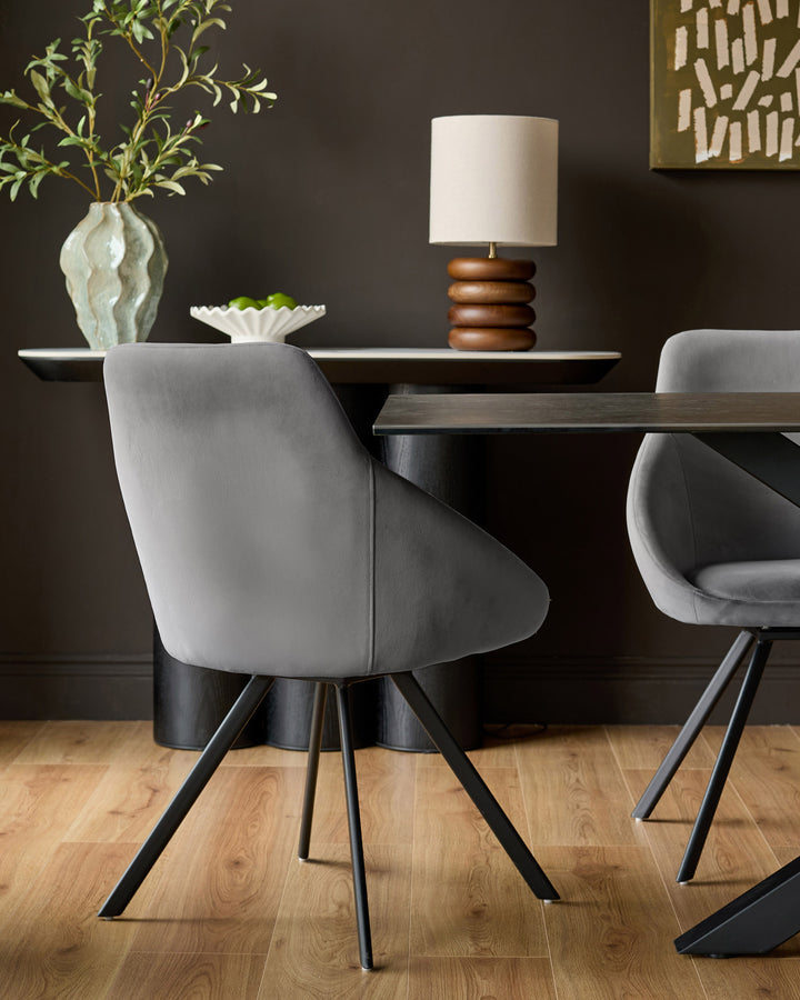 Cleo velvet swivel chair in dark grey with black metal legs, shown in a dining room setting.