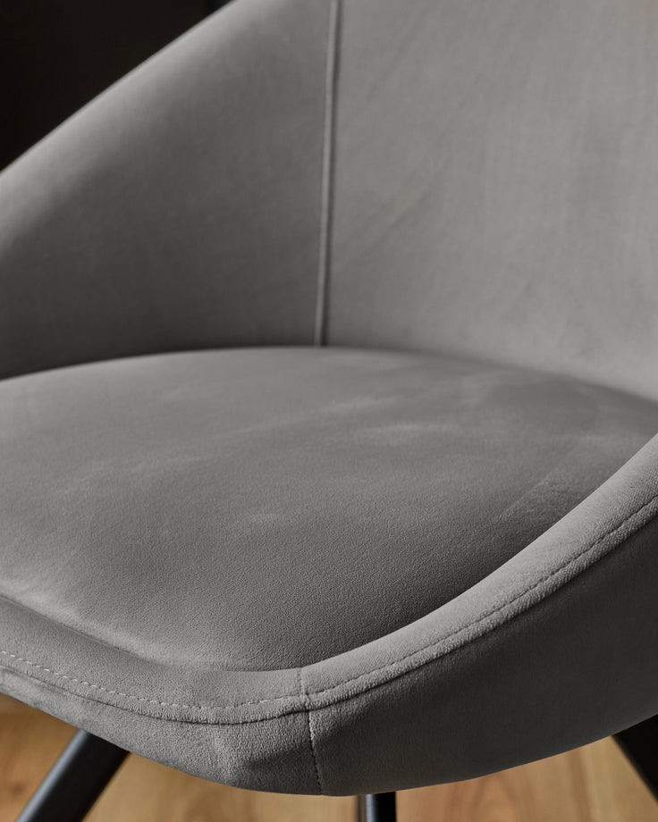 Cleo velvet swivel chair in dark grey, close-up of curved seat and backrest with stitched seams and wooden base.