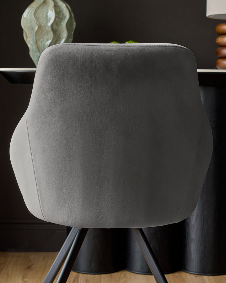 Cleo velvet swivel chair in dark grey, shown from back view with rounded backrest and black pedestal base on wooden floor.