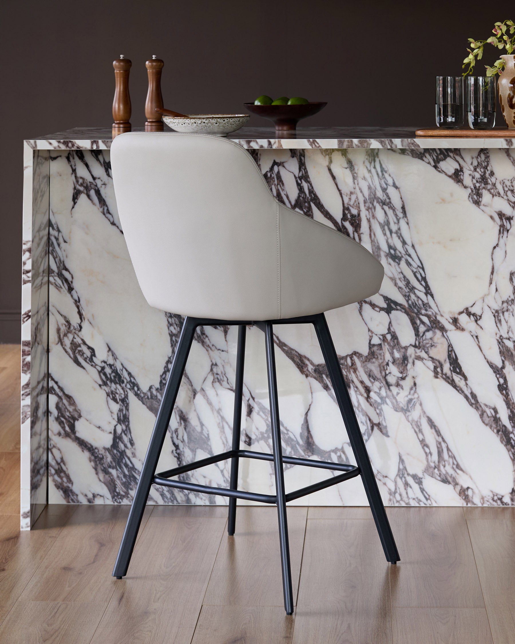 Cleo swivel bar stool in light grey faux leather with black metal legs, shown at marble counter.