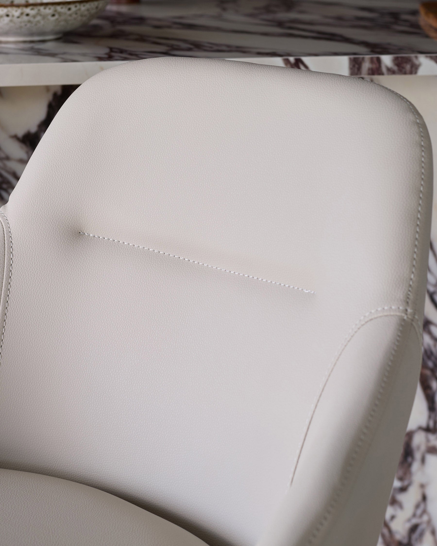 Cleo swivel bar stool in light grey faux leather, close-up of padded backrest with stitching detail.