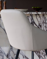 Cleo swivel bar stool in light grey faux leather, showing curved backrest and stitched seams from side angle.