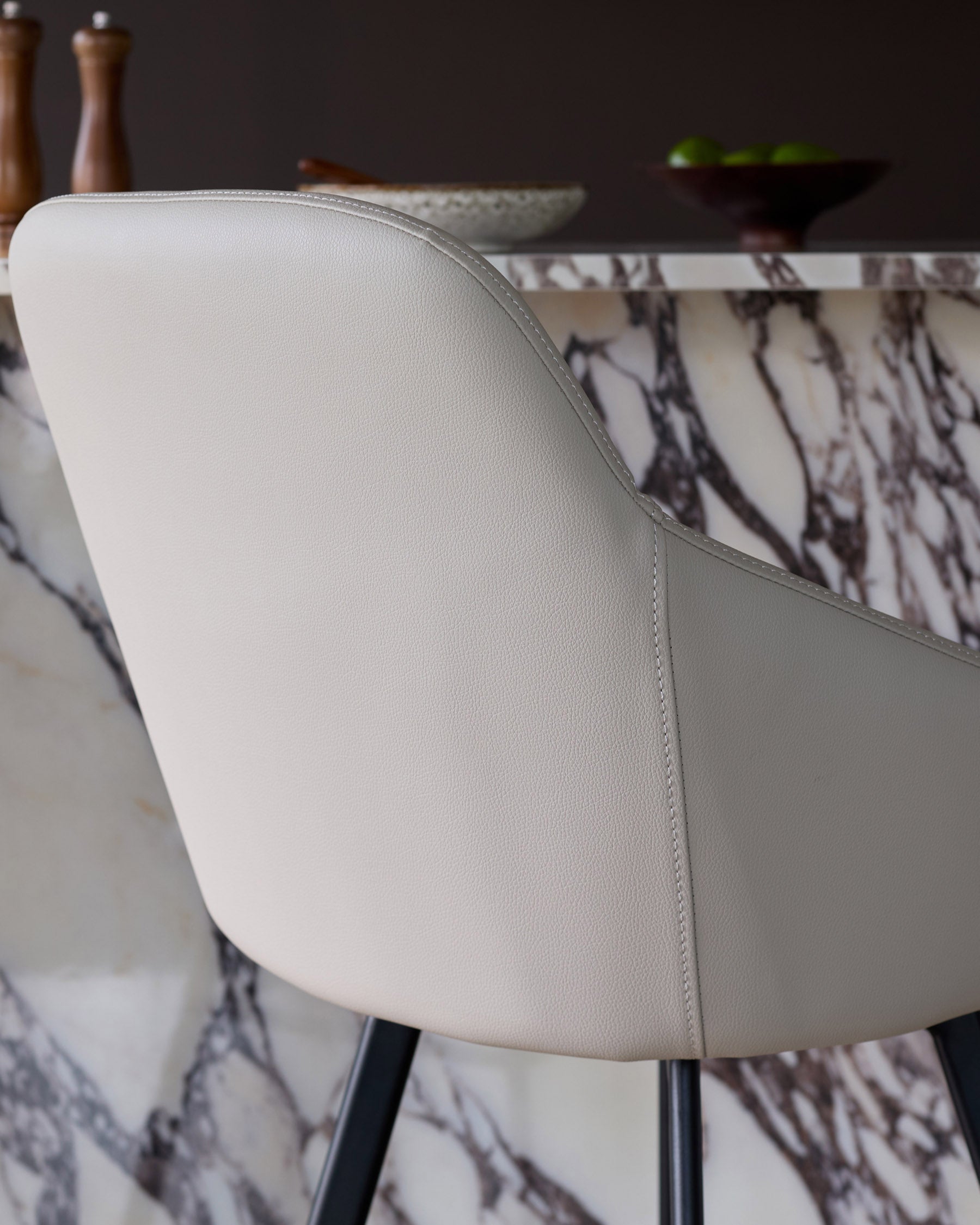 Cleo swivel bar stool in light grey faux leather, showing curved backrest and stitched seams from side angle.