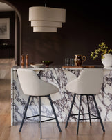 Cleo swivel bar stool in light grey faux leather with black metal legs, shown at marble kitchen island.