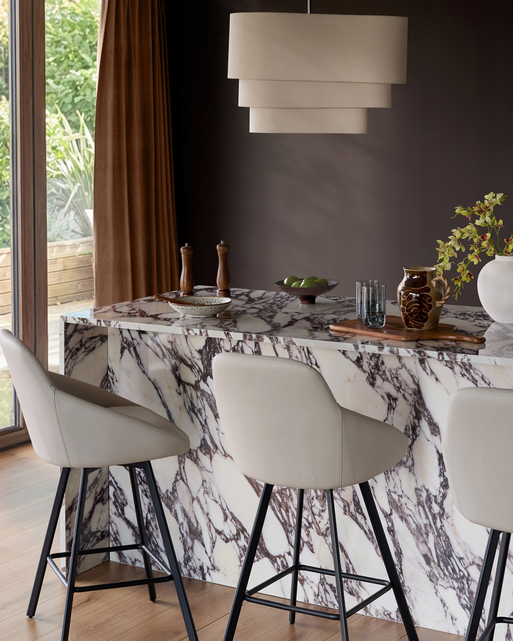 Cleo swivel bar stool in light grey faux leather with black metal legs, shown at marble counter in modern dining setting.