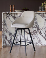 Cleo swivel bar stool in light grey faux leather with black metal legs, shown at a marble kitchen counter.