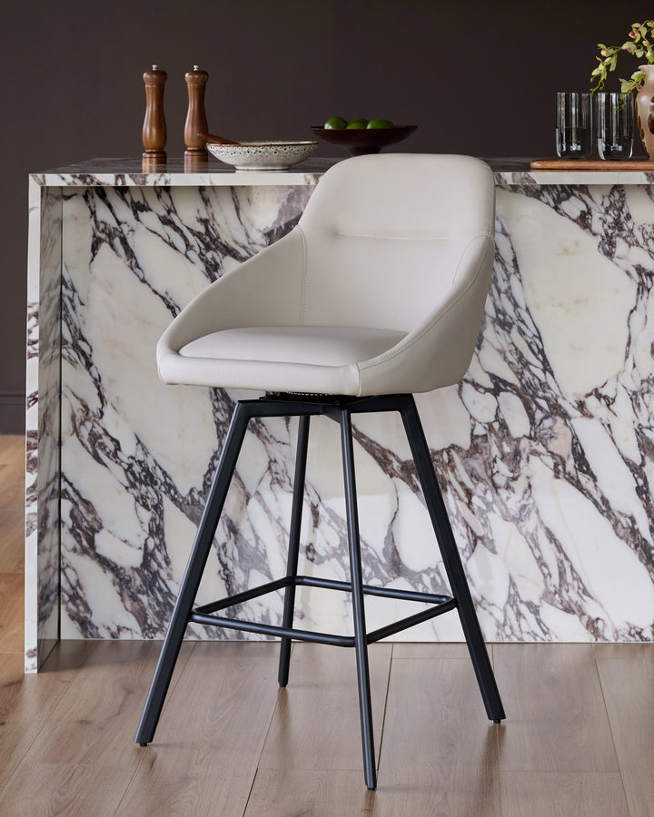 Cleo swivel bar stool in light grey faux leather with black metal legs, shown at a marble kitchen counter.