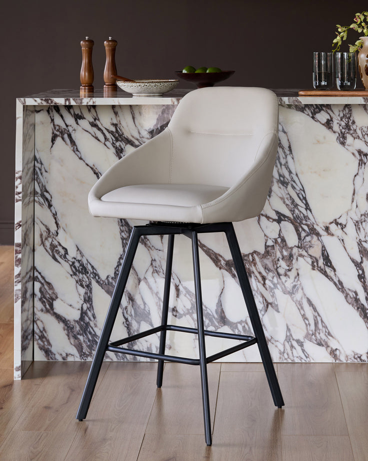 Cleo swivel bar stool in light grey faux leather with black metal legs, shown at a marble kitchen counter.