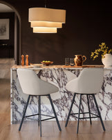 Cleo swivel bar stool in light grey faux leather with black metal legs, shown at marble kitchen island.