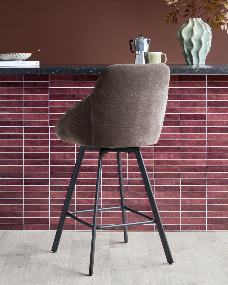 A stylish, grey fabric-covered bar stool with dark metal legs, perfect for a modern kitchen or bar area.
