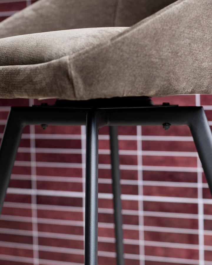 Close-up of a stylish chair with grey fabric and black metal legs against a brick wall.