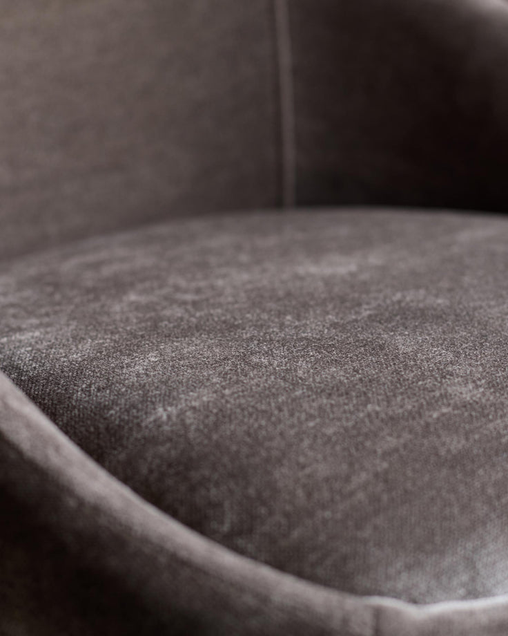 Close-up of a plush, curved chair in a warm, muted tone. The textured fabric seat invites relaxation.