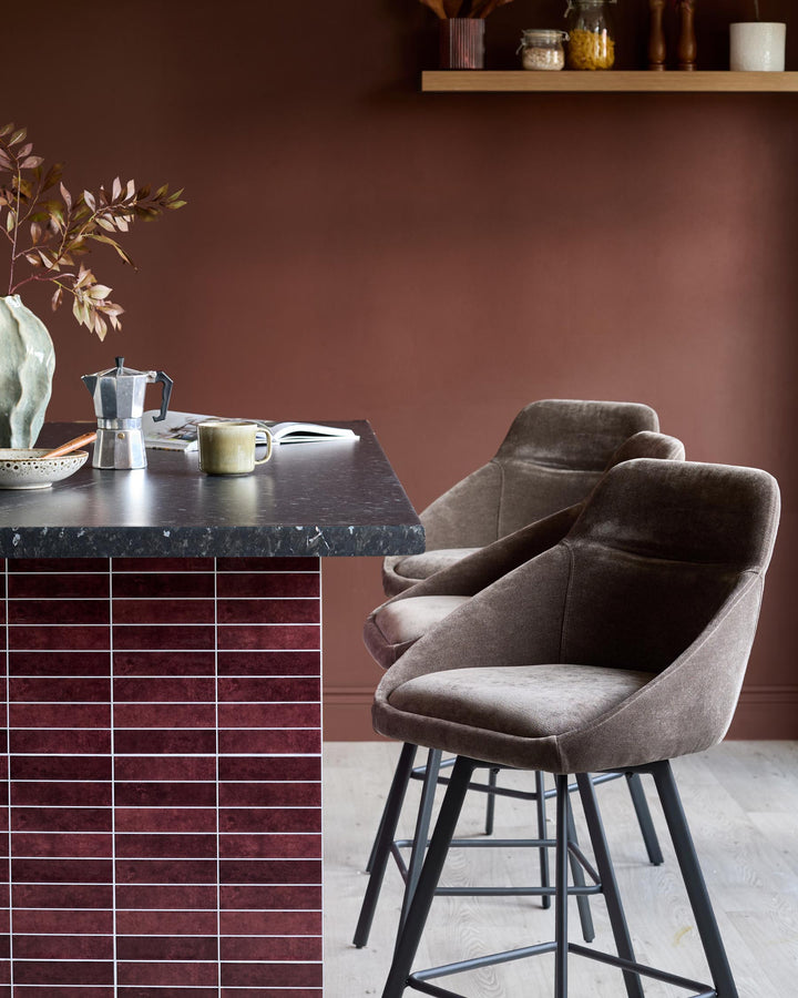 Stylish kitchen scene featuring two cushioned bar stools with black legs, positioned at a sleek, dark-topped breakfast bar.