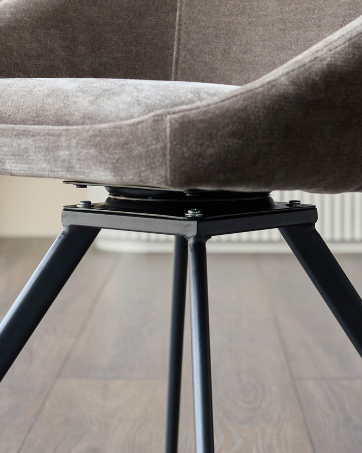 Close-up of a swivel chair with a grey upholstered seat and black metal legs, showing the base and leg structure.