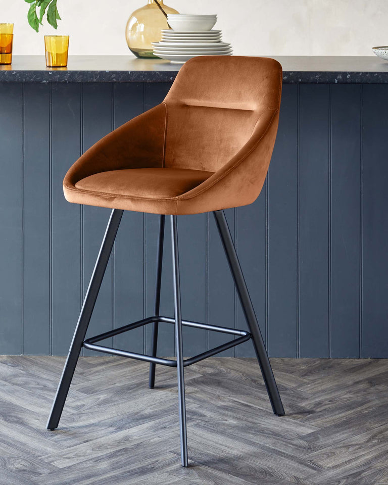 A contemporary bar stool with a caramel-coloured velvet seat and a black metal frame set against a dark panelled wall and wood-patterned flooring.
