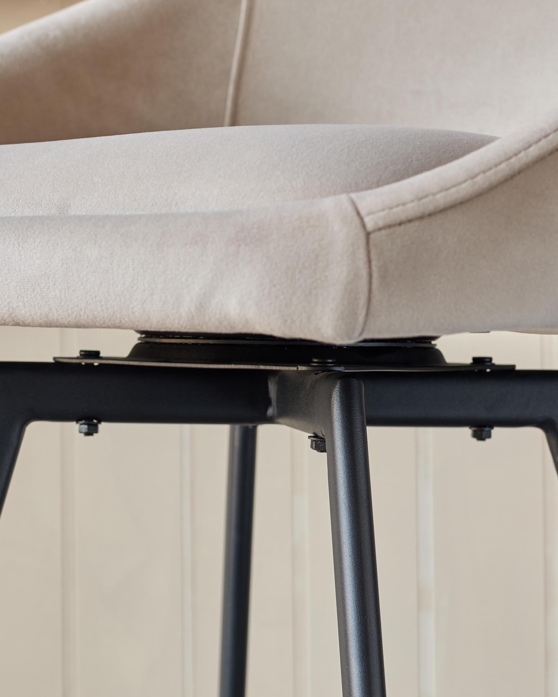 A swivel chair with neutral fabric and a black metal frame and legs is shown in a close-up, cropped view.