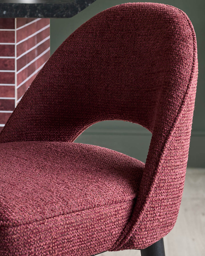 Close-up of a stylish, upholstered chair in a rich burgundy fabric, featuring a curved back with a distinctive cut-out design.