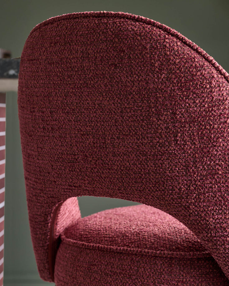 Close-up of a wine-coloured upholstered chair, showcasing its curved back and textured fabric.