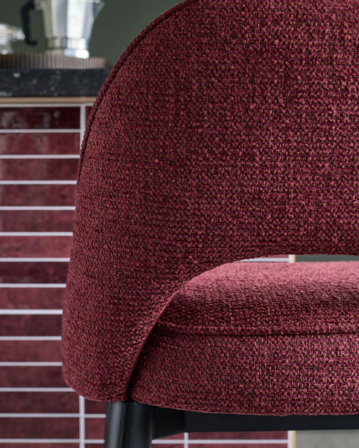 Close-up of a stylish red upholstered chair with a curved backrest, offering a textured and inviting seating option.