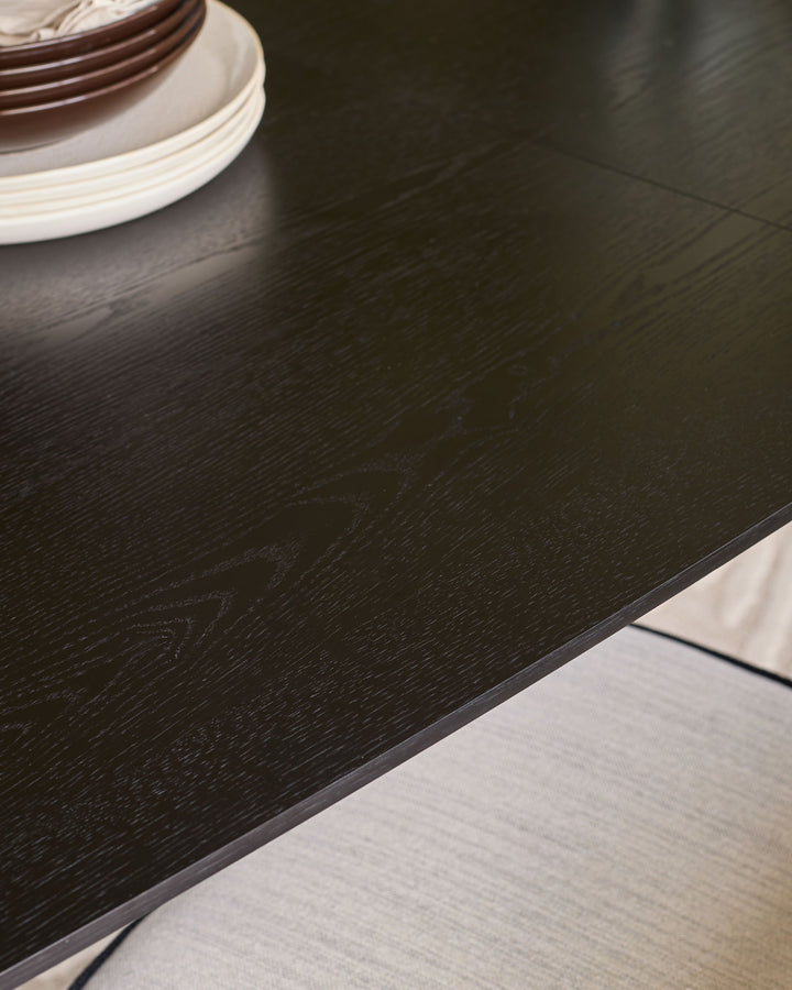 Black wood extending dining table with natural grain texture and light-colored base visible at edge.