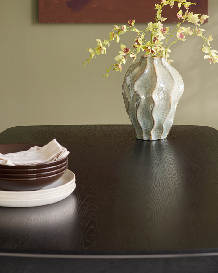 Black wood extending dining table with wavy edge detail, styled with stacked plates and floral arrangement.