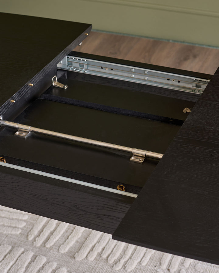Black wood extending dining table with open leaf mechanism and polished metal handles, shown at an angle.