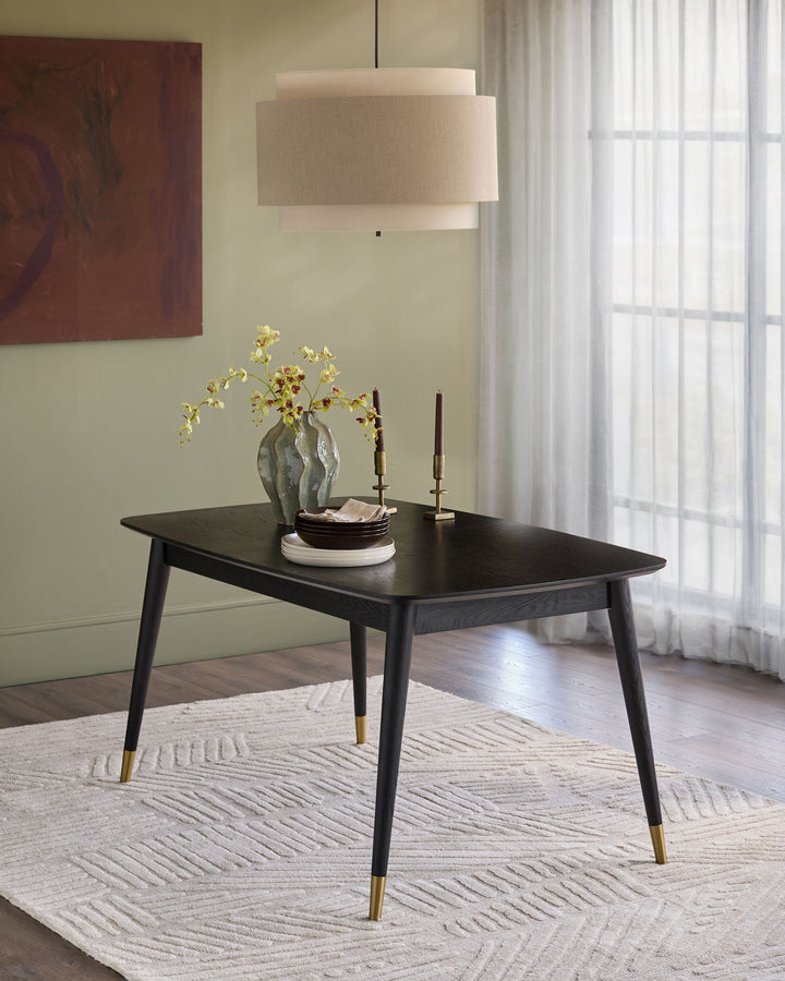 Black extending dining table with tapered legs and brass feet caps, styled in a contemporary room setting.
