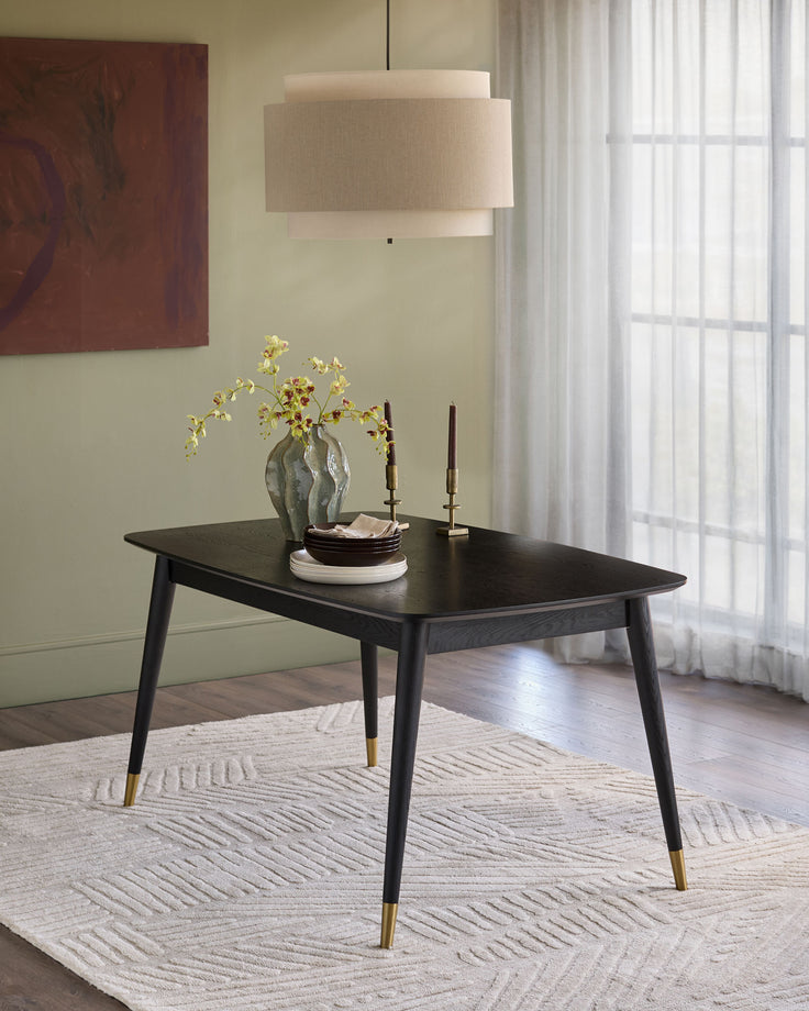 Black extending dining table with tapered legs and brass feet caps, styled in a contemporary room setting.