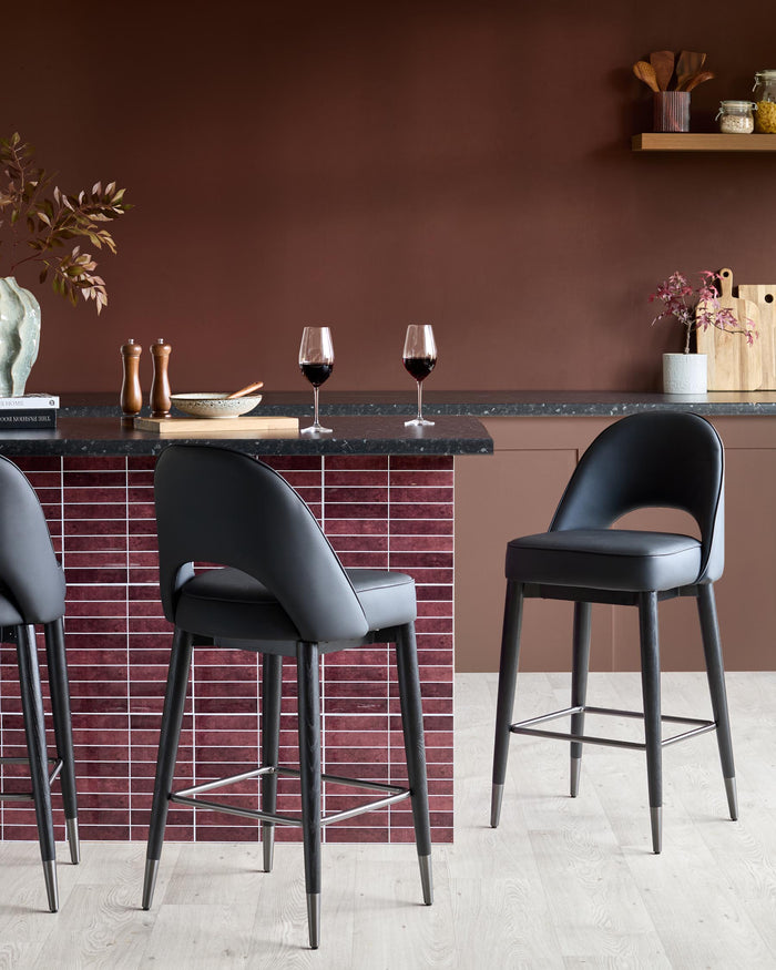Stylish kitchen island with black granite worktop and sleek black bar stools on a light wooden floor.